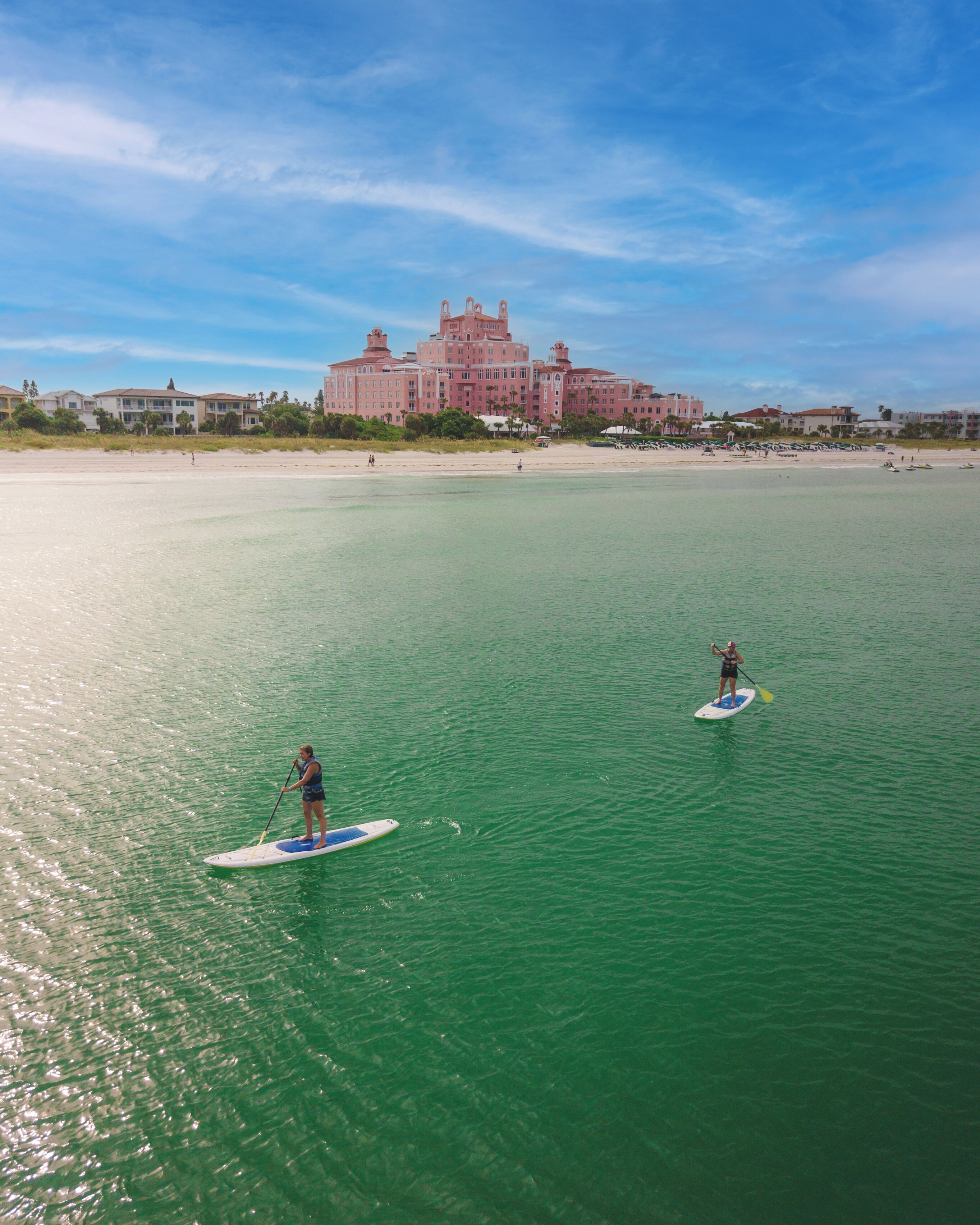 Een groot resort met uitzicht op het strand, paddleboarders op het water, en een heldere lucht.
