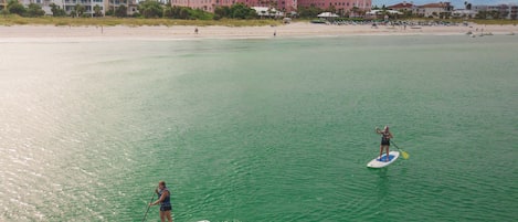 A large resort with a beach view, paddleboarders on the water, and a clear sky.
