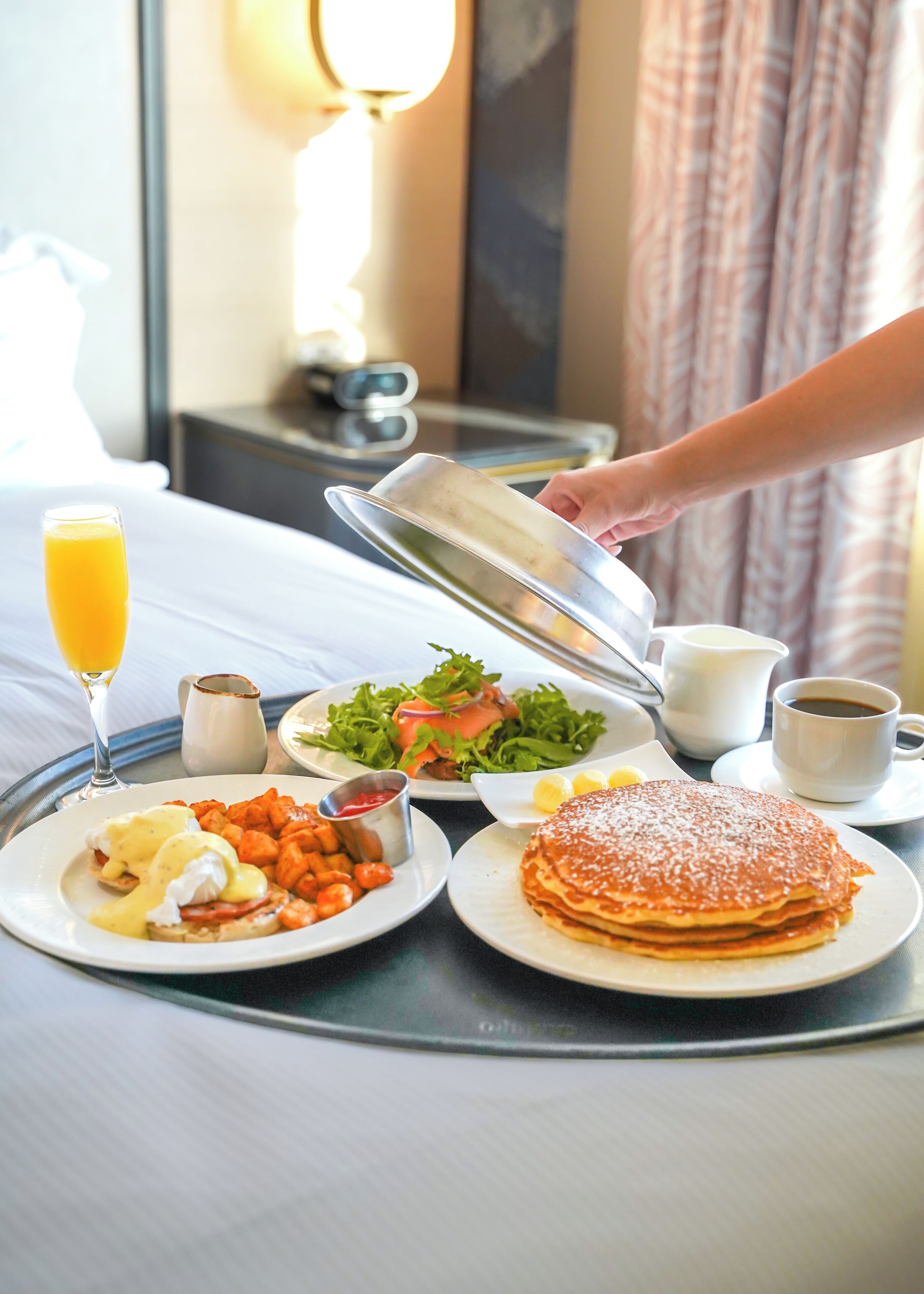 A breakfast table with plates of eggs benedict, waffles, and a glass of orange juice.