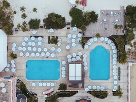 Una vista aerea di un resort con due piscine, lettini e ombrelloni.