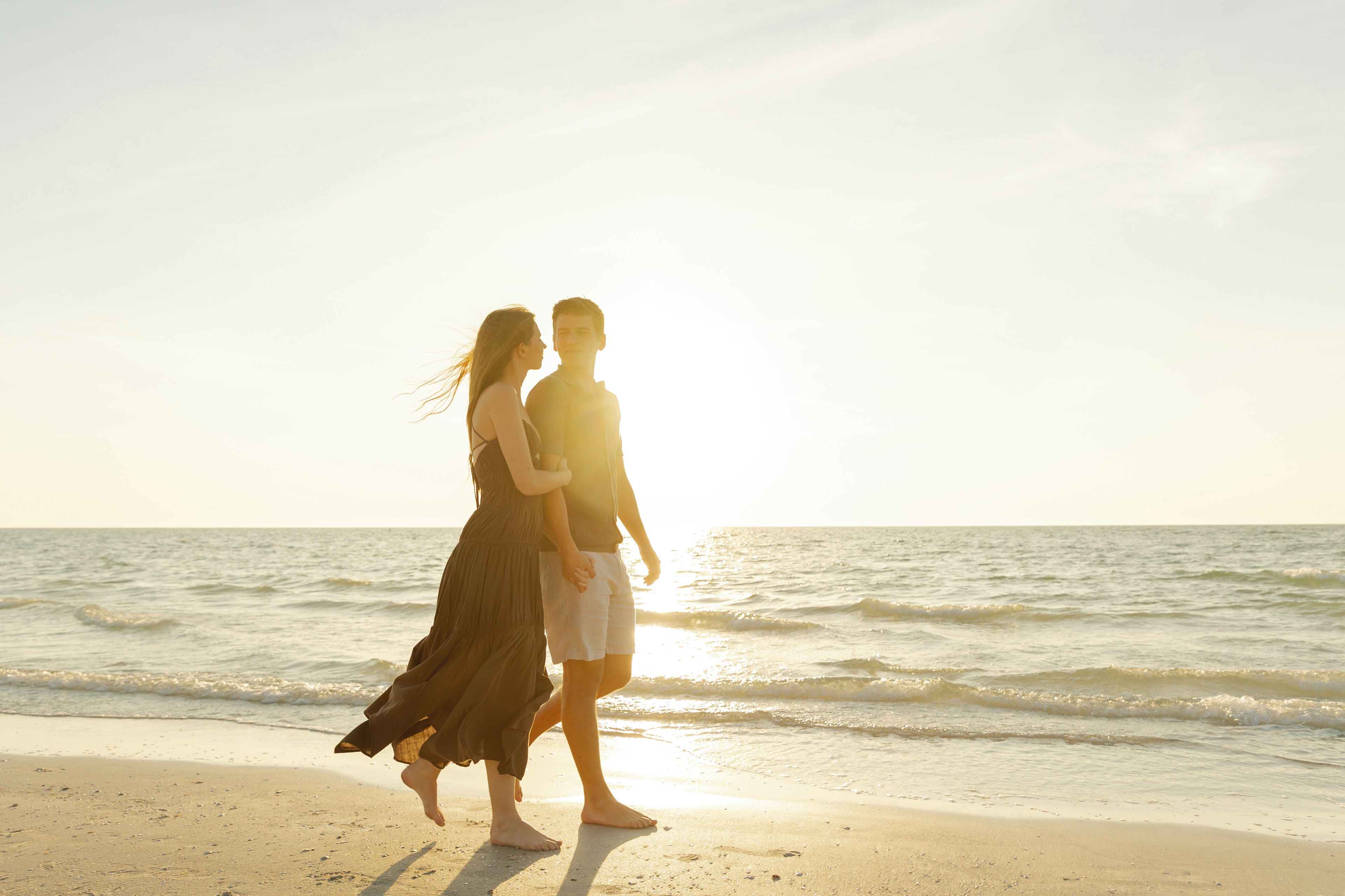 A couple walking on a beach with the ocean in the background.