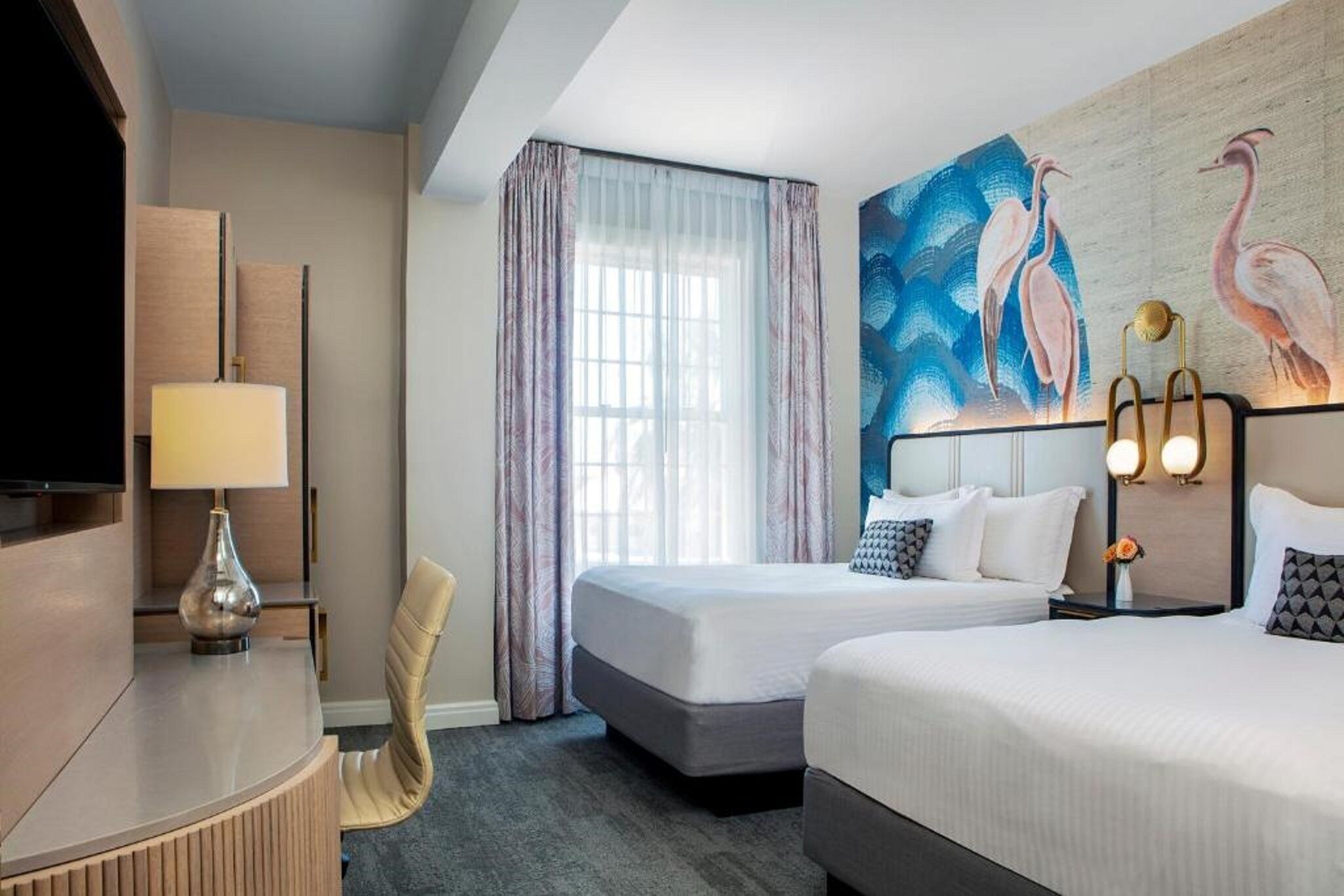 A hotel room with two beds, a desk, a chair, a TV, and a painting on the wall.