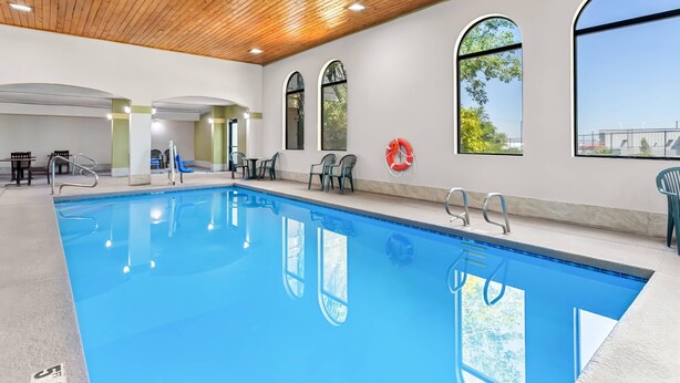 Una piscina con acqua cristallina, circondata da sedie e un salvagente appeso al muro.