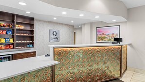 Un'area della reception di un hotel con un bancone bianco, un cartello 'Quality by Choice Hotels' e una televisione montata a parete, oltre a scaffali con snack.