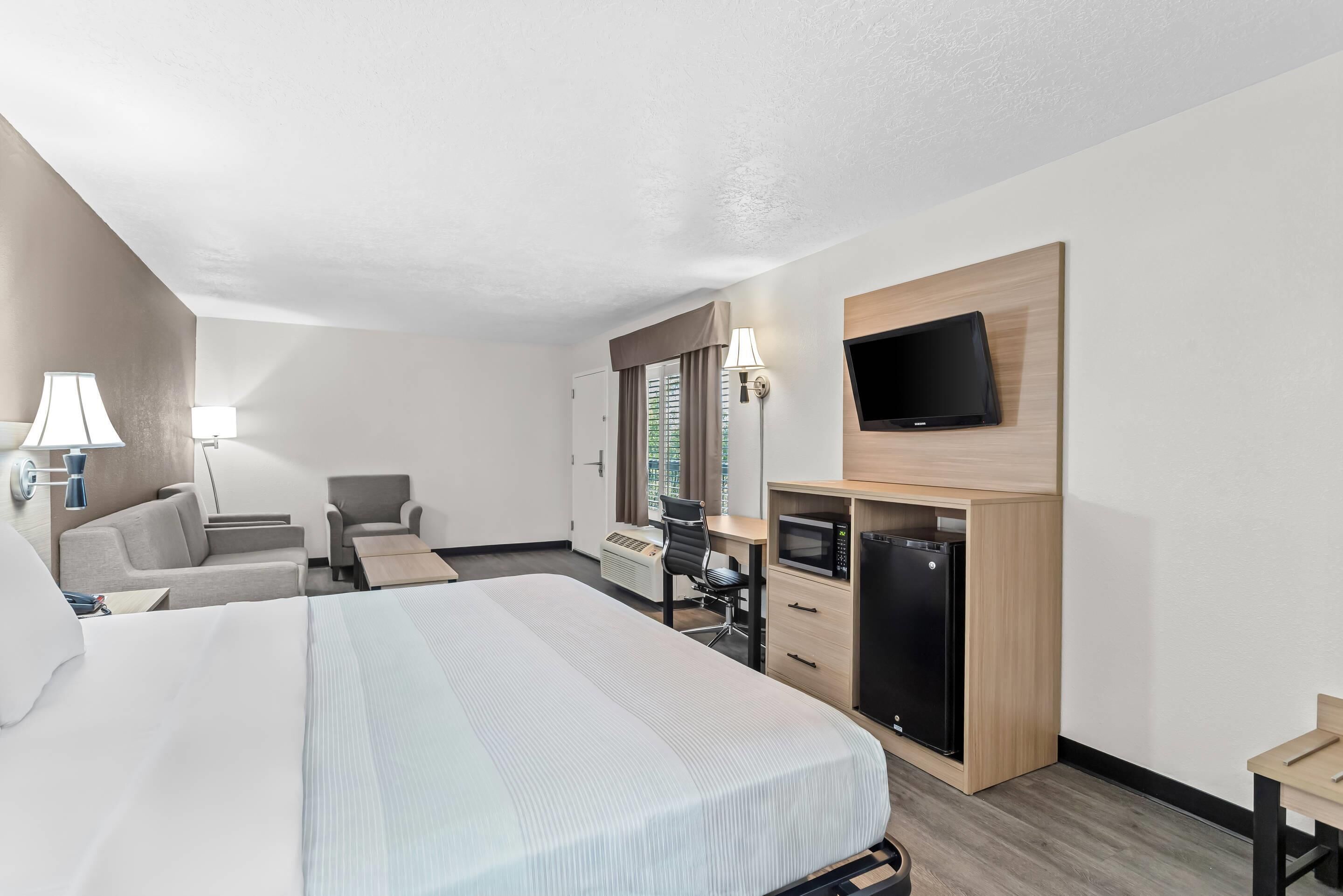 A hotel room with a large bed, a desk, a chair, a TV, and a minibar.