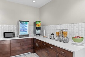 Una cocina moderna con refrigerador, microondas, cafetera y dispensador de cereales.