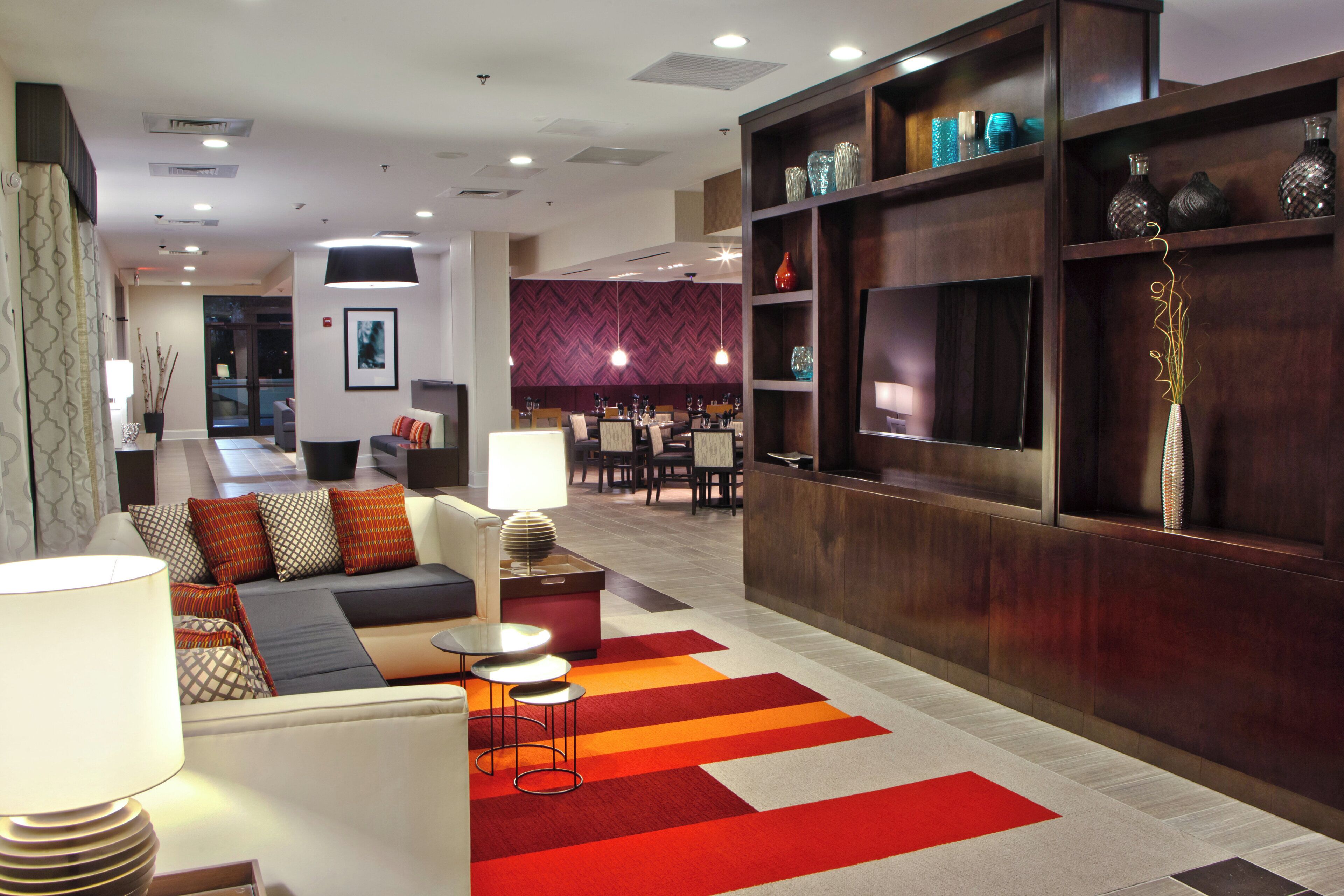 A hotel lobby with a seating area, a reception desk, and a dining area.