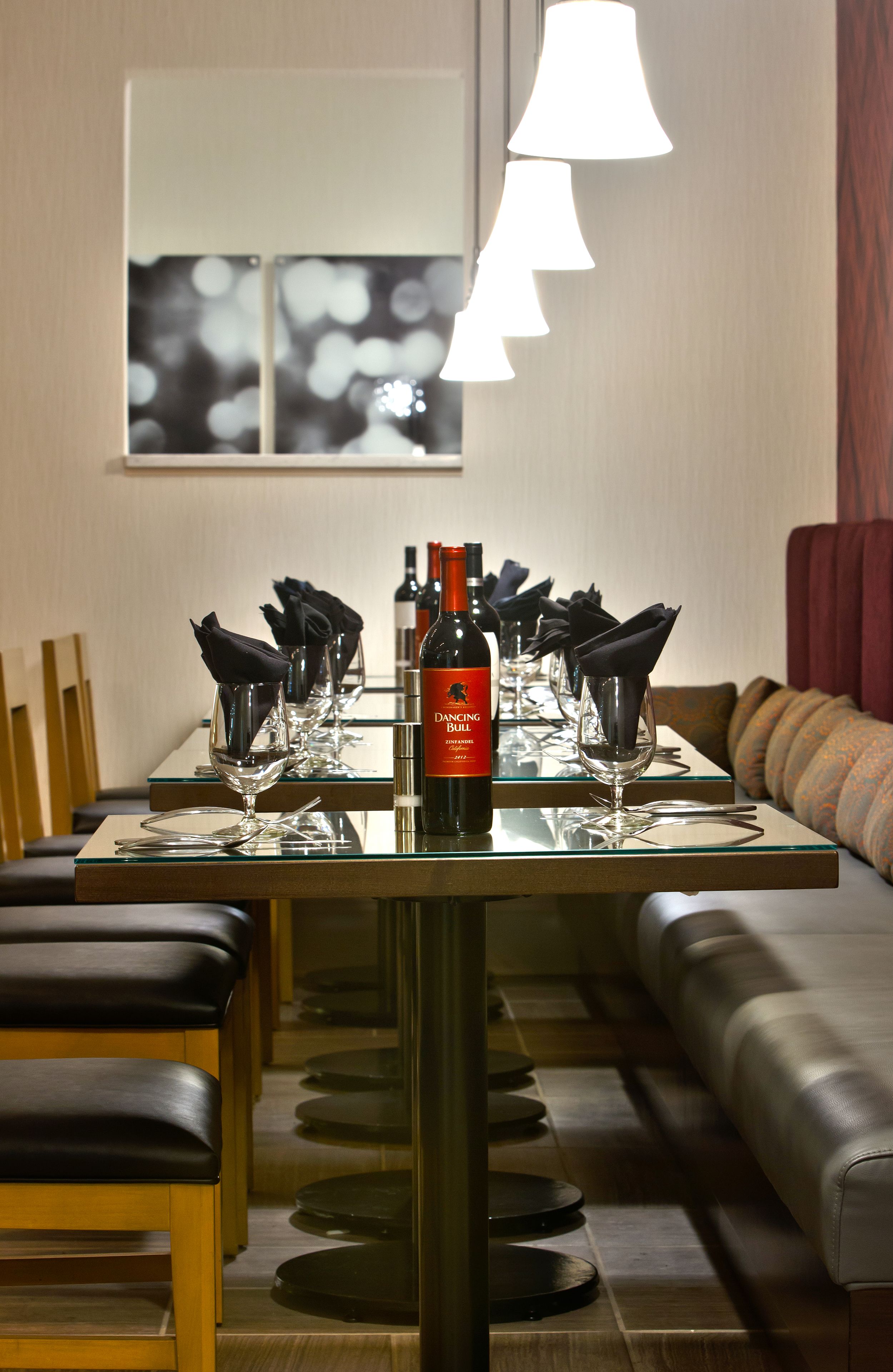 Mesa de comedor dispuesta con copas de vino, una botella y servilletas negras.