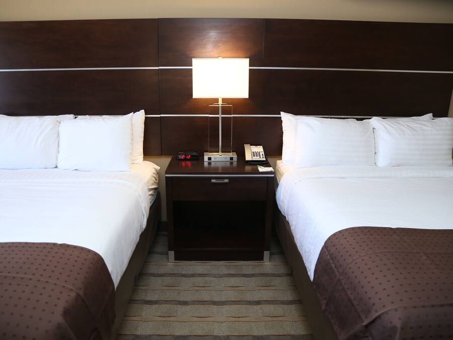 A hotel room with two beds, a nightstand with a lamp, a clock, and a phone.