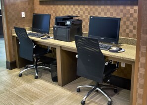 A workspace with two desks, each equipped with a computer monitor, keyboard, and mouse. There are two printers on the desks, and the room has a tiled floor and wooden paneling on the walls. - Holiday Inn Charlotte Airport by IHG (Charlotte)