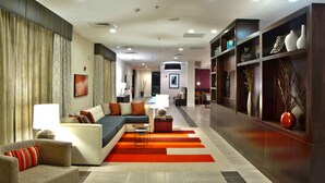 Un moderno vestíbulo de hotel con un sofá, sillones, zona de comedor y una estantería con adornos.