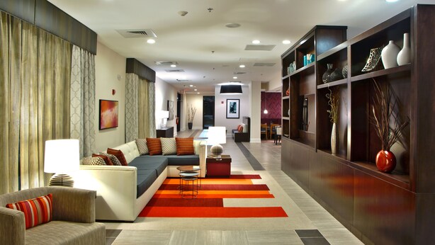 Un hall d’hôtel moderne comprenant un canapé, des fauteuils, un coin repas et une bibliothèque agrémentée d’objets décoratifs.