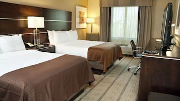 A hotel room with two beds, a desk, a chair, a TV, and a window with curtains.