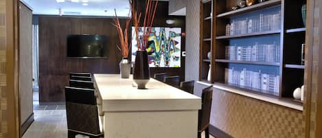Una cocina moderna con una isla central, taburetes de bar, un televisor de pantalla plana y una estantería con objetos decorativos.