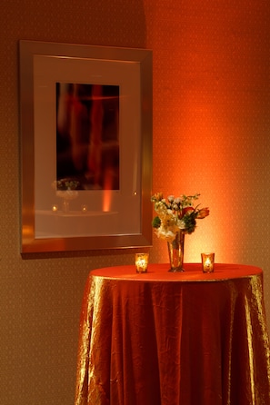 A framed picture on a wall, a table with a red tablecloth, and a vase with flowers.