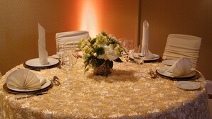 Una mesa redonda con un centro de mesa floral blanco, mantel blanco y vajilla dispuesta con cuidado.