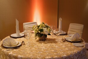 A round table with a white floral centerpiece, white tablecloth, and neatly arranged dinnerware. - Holiday Inn Charlotte Airport by IHG (Charlotte)