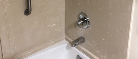 A bathroom with a bathtub, a shower, and a handrail.