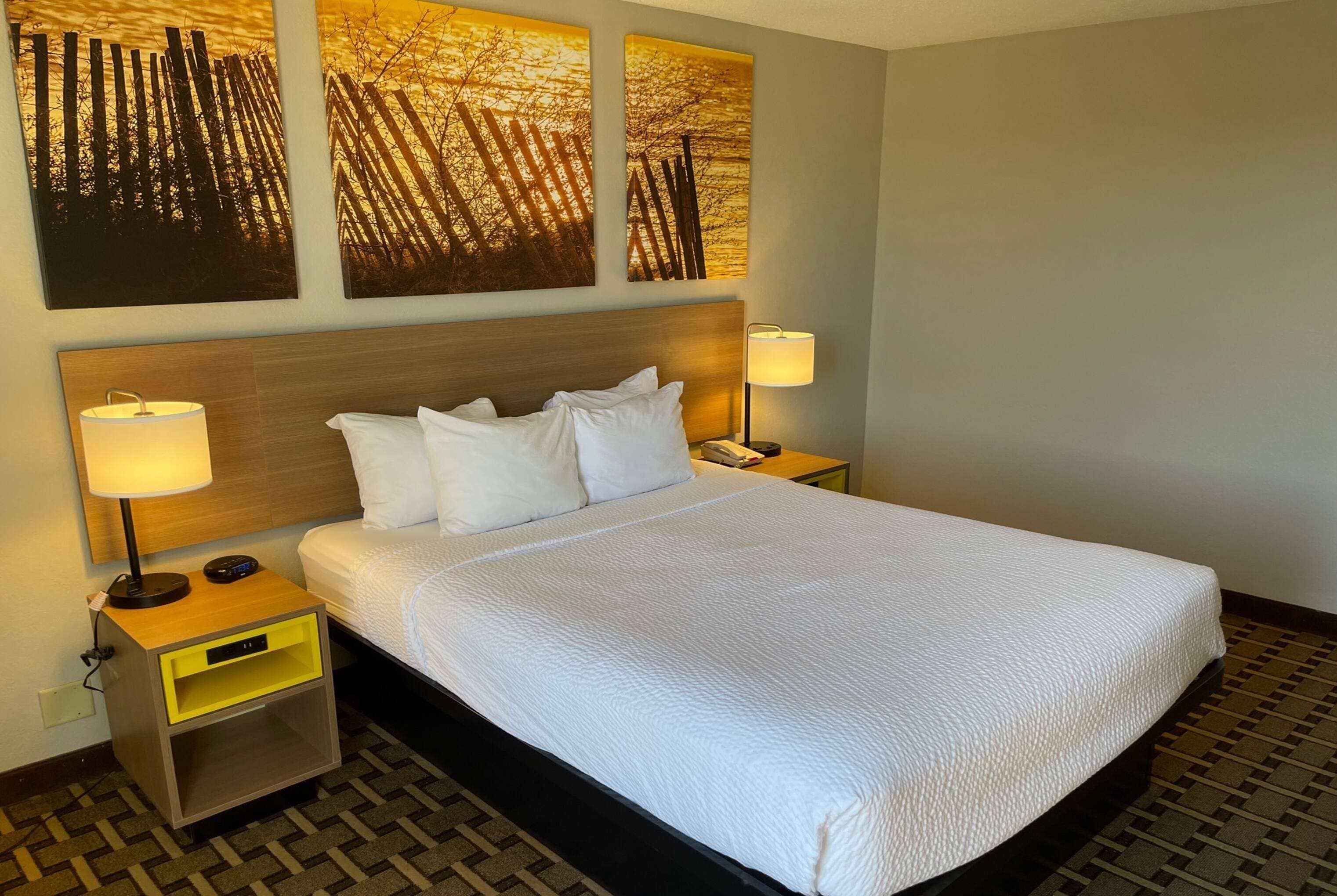 A neatly made bed with white linens, a wooden headboard, and two bedside lamps.
