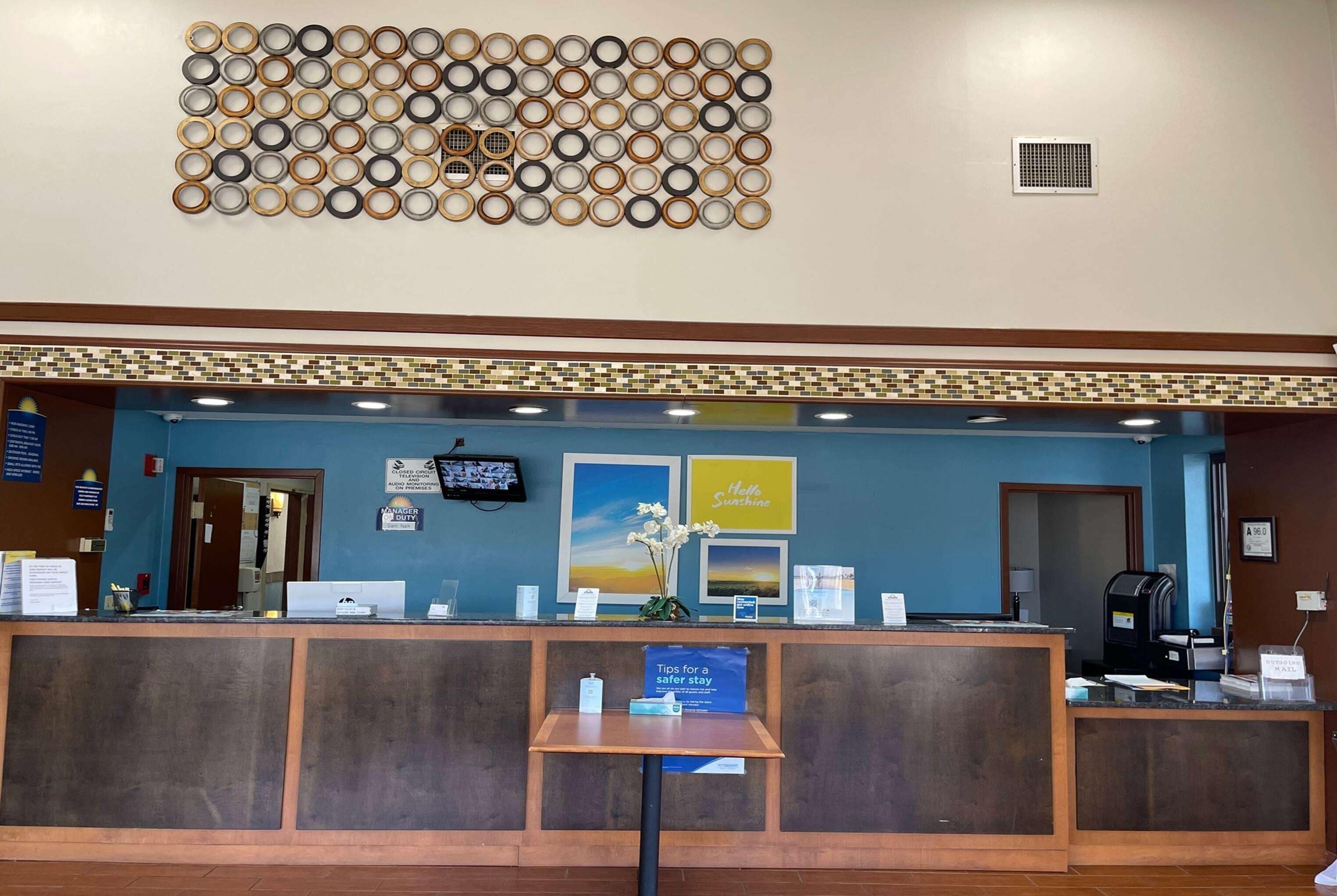 A reception desk with a blue wall, a decorative wall art piece above, and a sign with tips for a safer stay.
