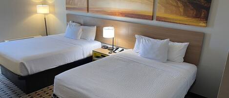 A hotel room with two beds, a nightstand with a lamp, and a painting on the wall.