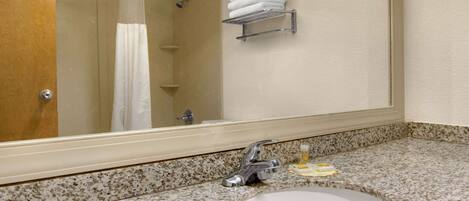A bathroom with a granite countertop, a sink, a mirror, a towel rack, and a shower.