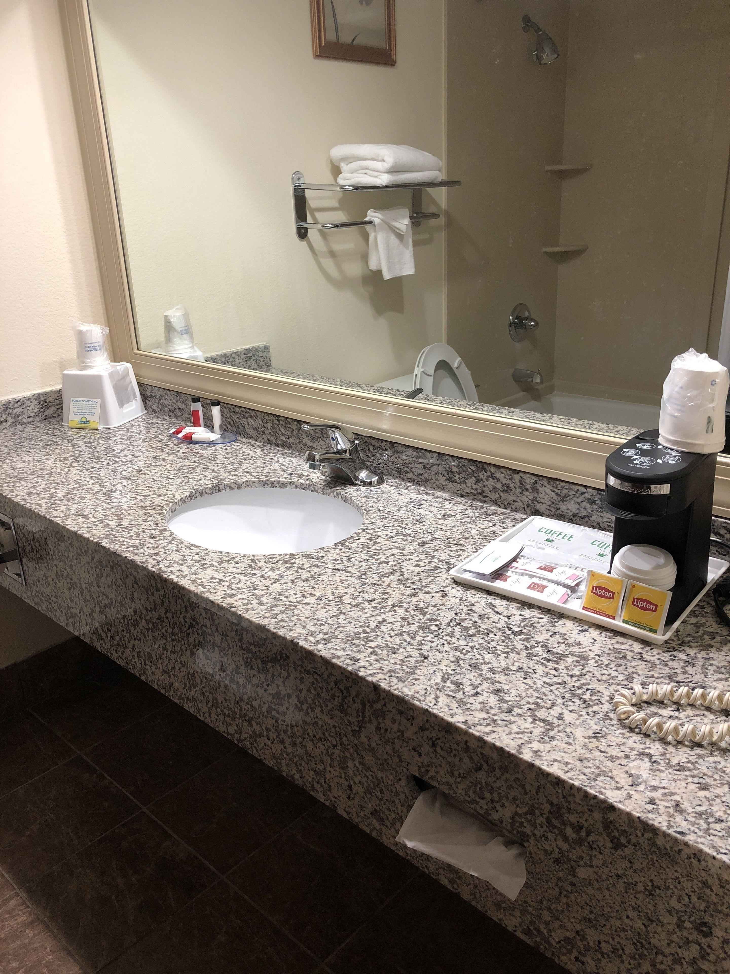 Une salle de bain avec un comptoir en granit, un lavabo, un miroir, un porte-serviettes, une douche et une machine à café.