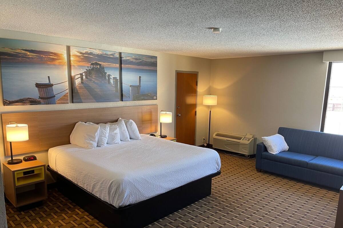 Une chambre d’hôtel avec un grand lit, un canapé bleu, un tableau représentant une jetée et une lampe.