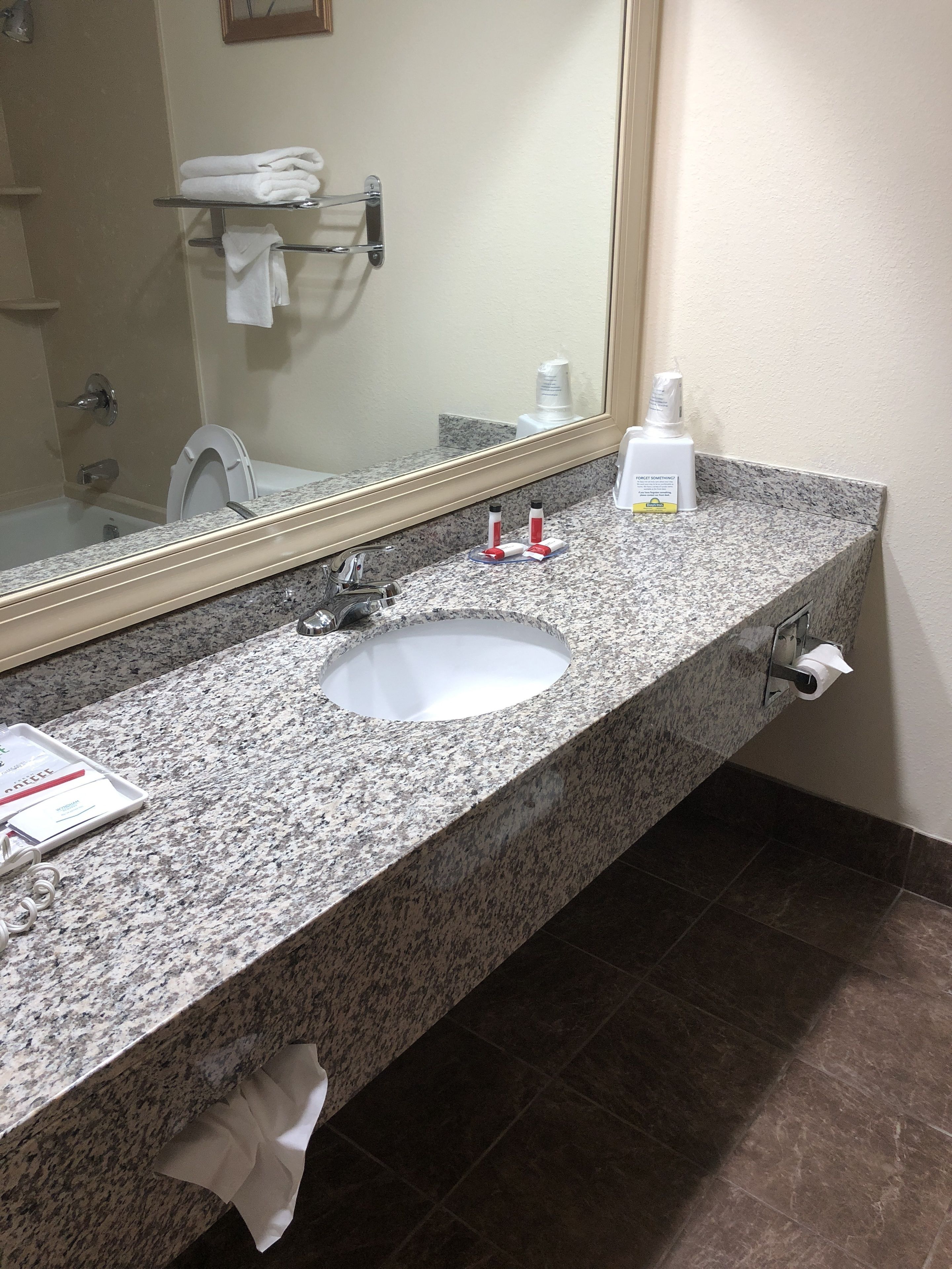 A bathroom with a granite countertop, a white sink, a mirror, and a towel rack.