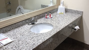 A bathroom with a granite countertop, a white sink, a mirror, and a towel rack.