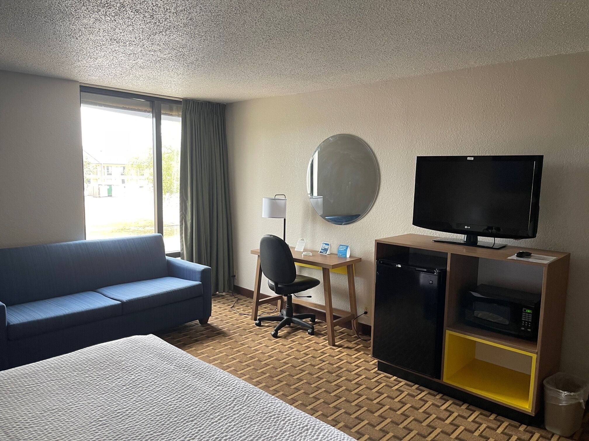 A hotel room with a bed, a blue sofa, a desk with a computer, a television, and a minibar.