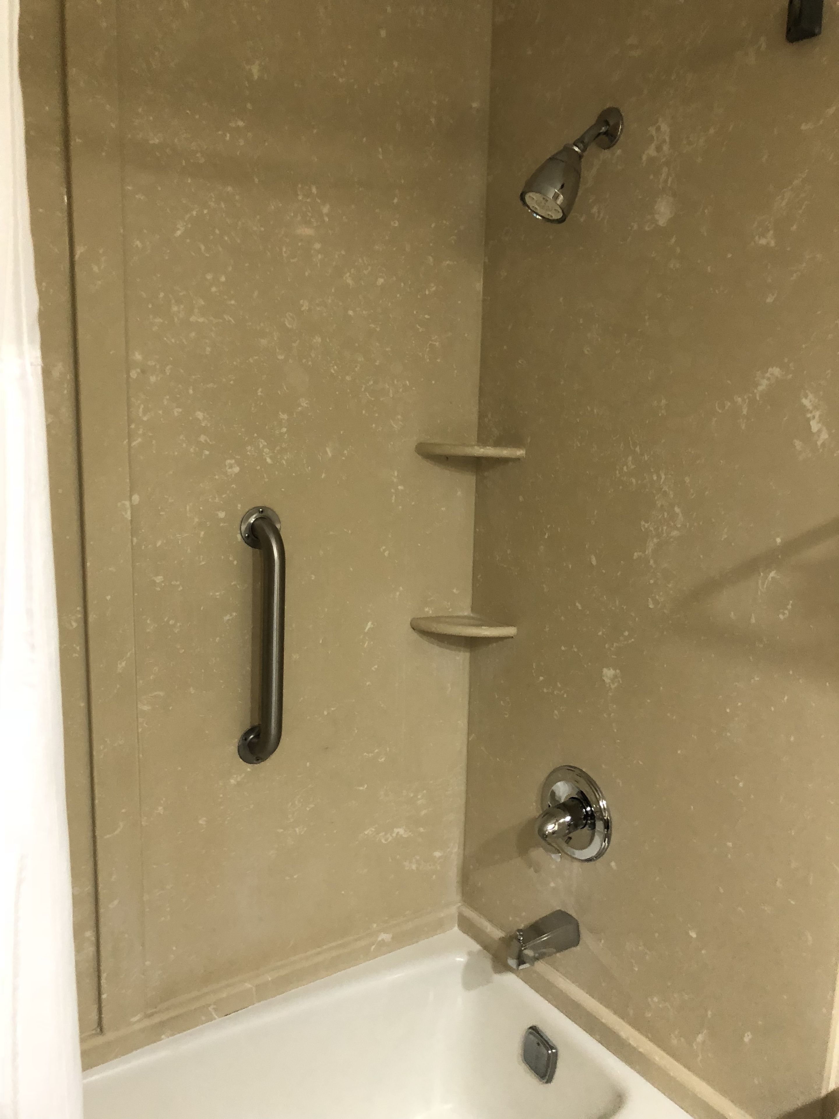 A bathroom with a bathtub, a shower, and a handrail.