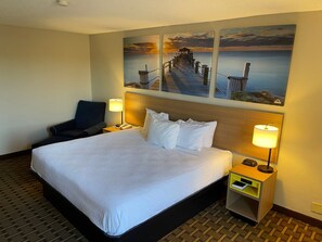 A hotel room with a large bed, two bedside tables, a chair, and artwork depicting a pier and sunset.