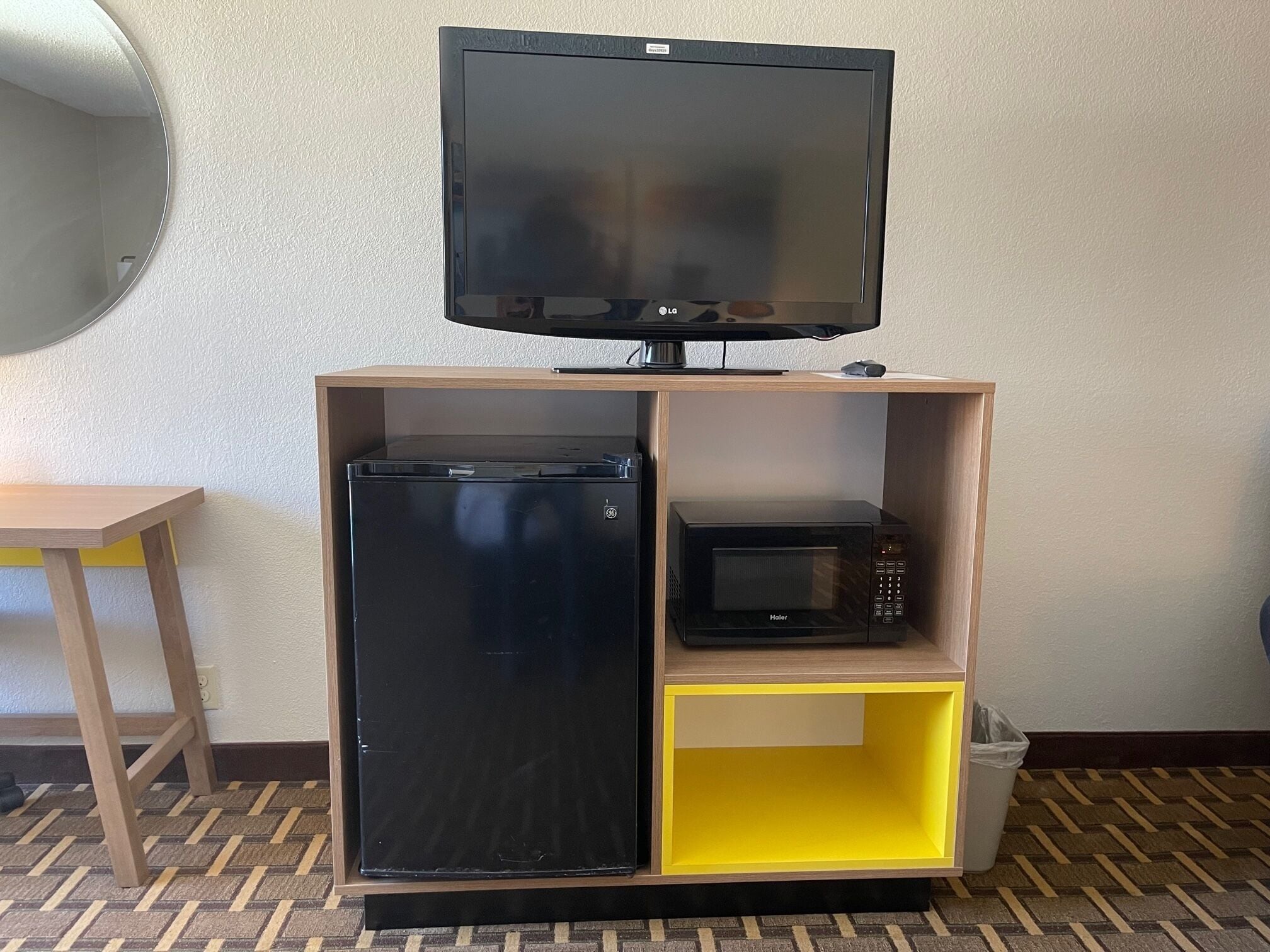 A compact kitchenette with a refrigerator, microwave, and a flat-screen TV on a wooden shelf unit.