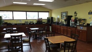 Un restaurante con mesas y sillas de madera, una zona de cocina y un cartel que anuncia desayuno.