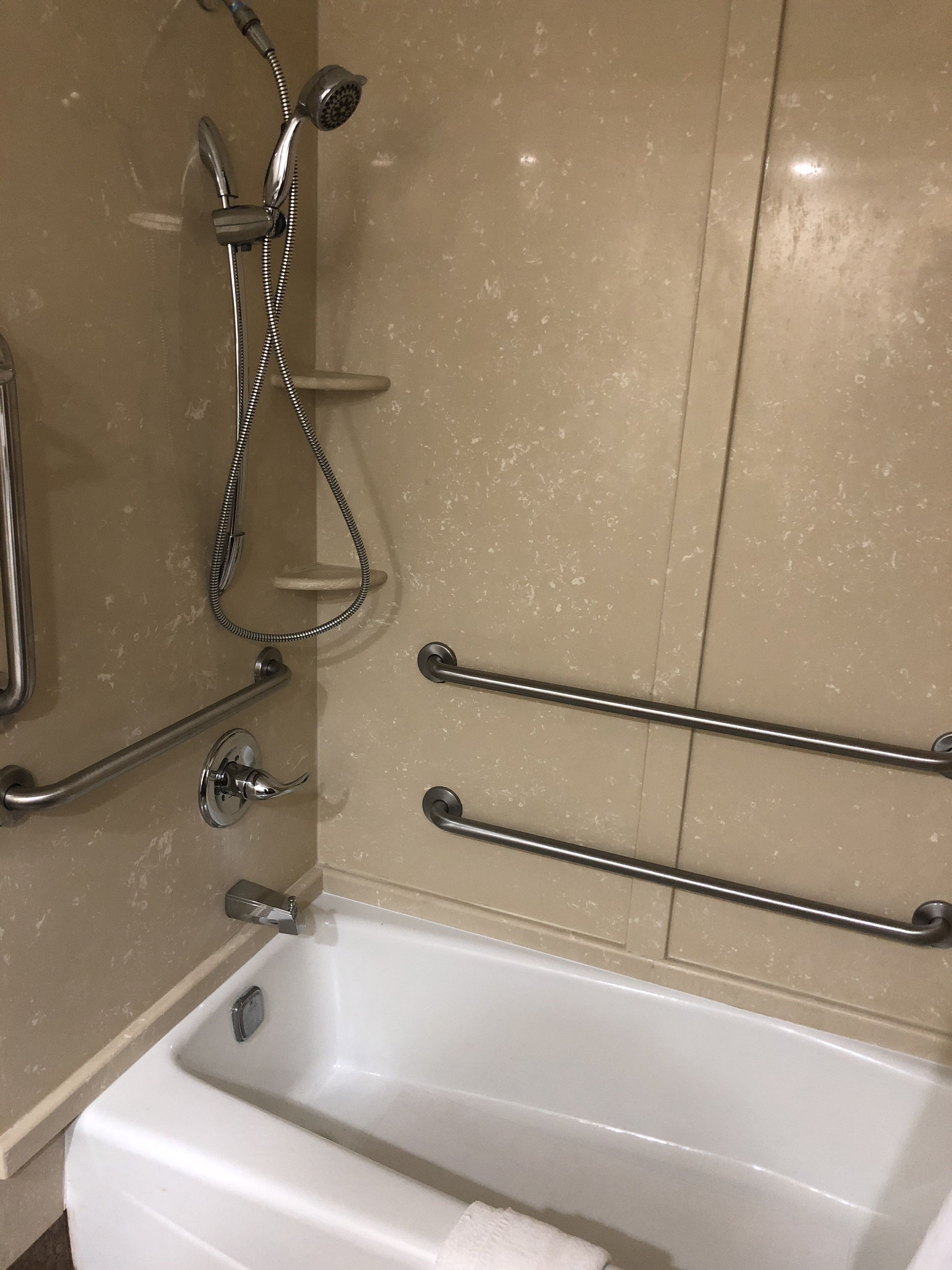 A bathroom with a white bathtub, a handheld showerhead, and two grab bars.