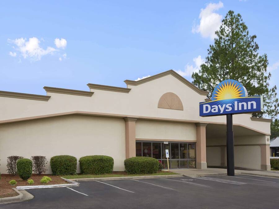 Um hotel Days Inn com fachada bege, estacionamento e céu claro.