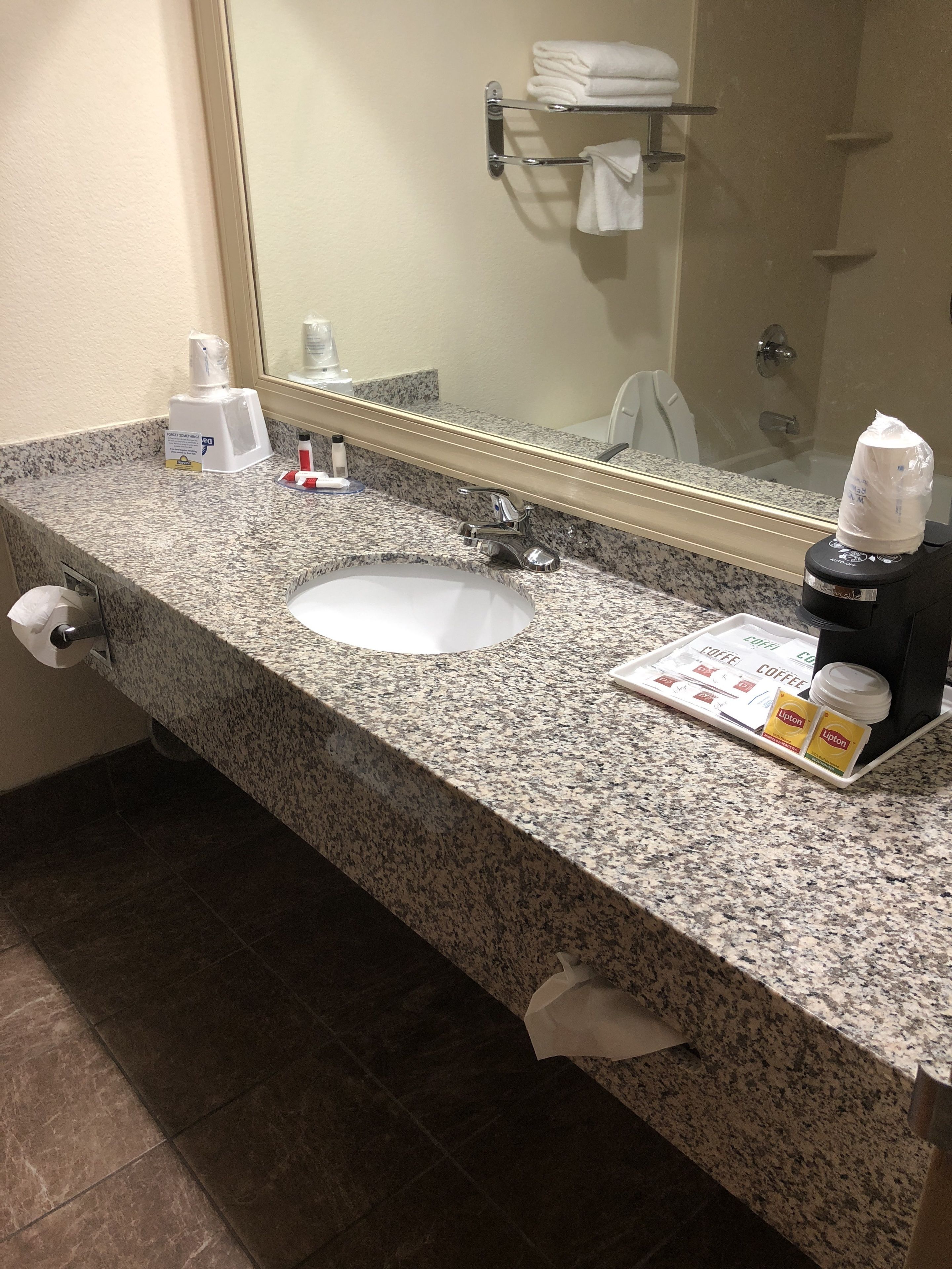 A bathroom with a granite countertop, a sink, a mirror, a towel rack, and toiletries.
