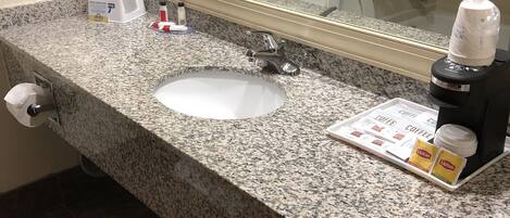 A bathroom with a granite countertop, a sink, a mirror, a towel rack, and toiletries.