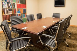 Conference room with a large table and comfortable seating for eight, featuring a bookshelf and flat-screen TV.