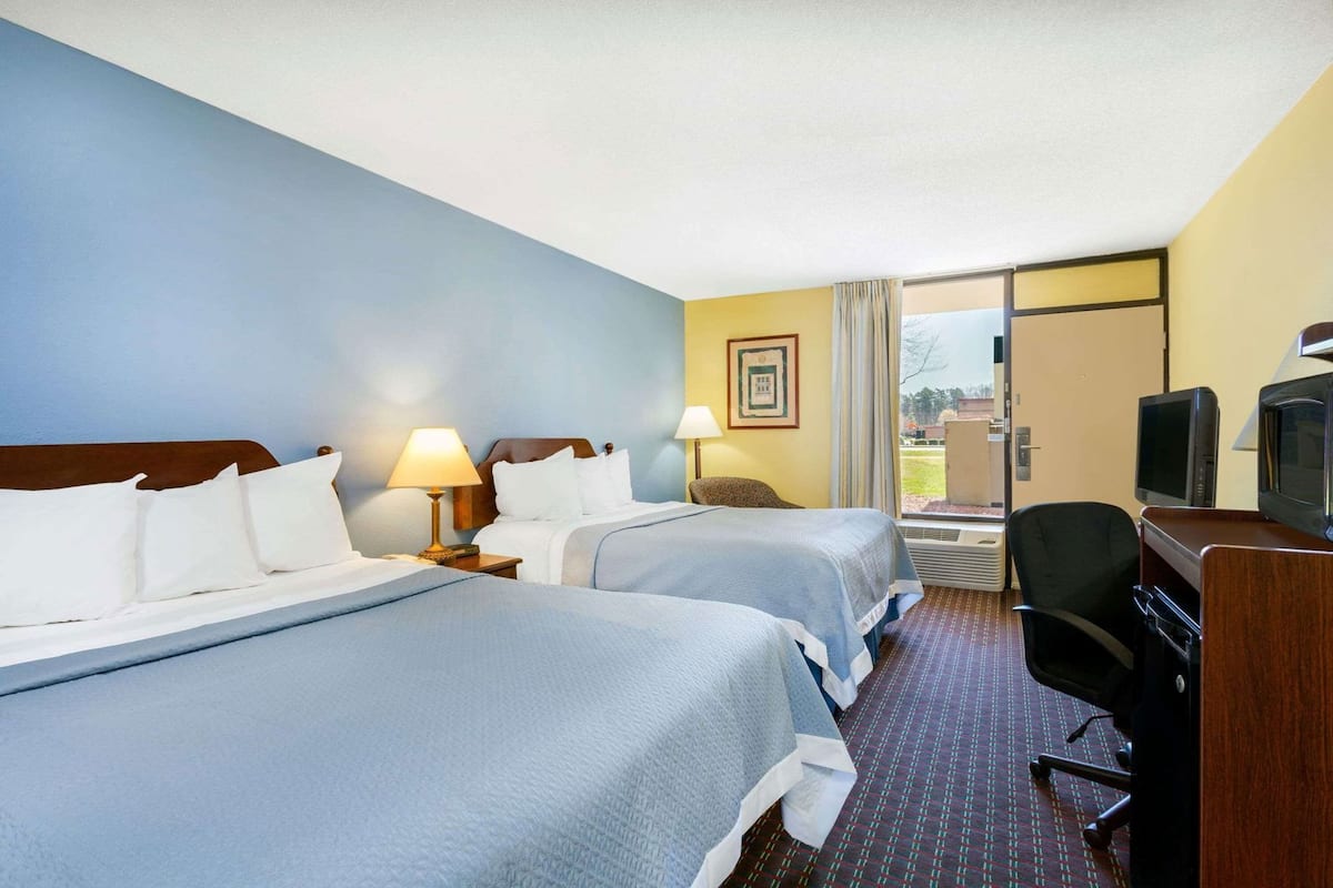 A hotel room with two beds, a desk, a chair, a television, and a window with a view.