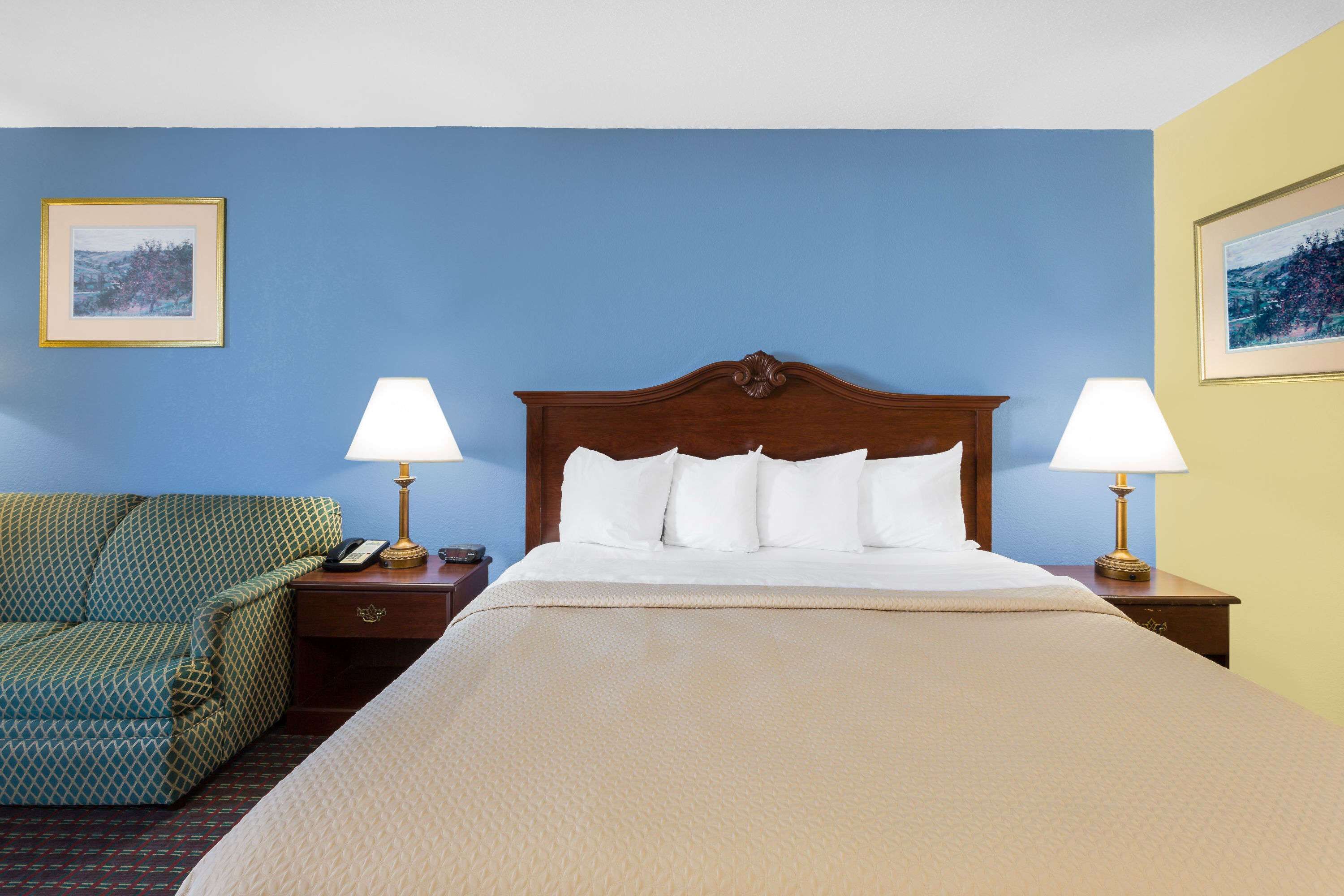 Un cuarto de hotel con una cama grande, dos lámparas de noche, un sofá verde con estampado y dos cuadros en las paredes.