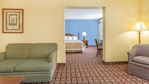 A hotel room with a patterned carpet, a green sofa, a bed with white linens, a nightstand with a lamp, and a framed picture on the wall. - Days Inn by Wyndham Mocksville (Mocksville)