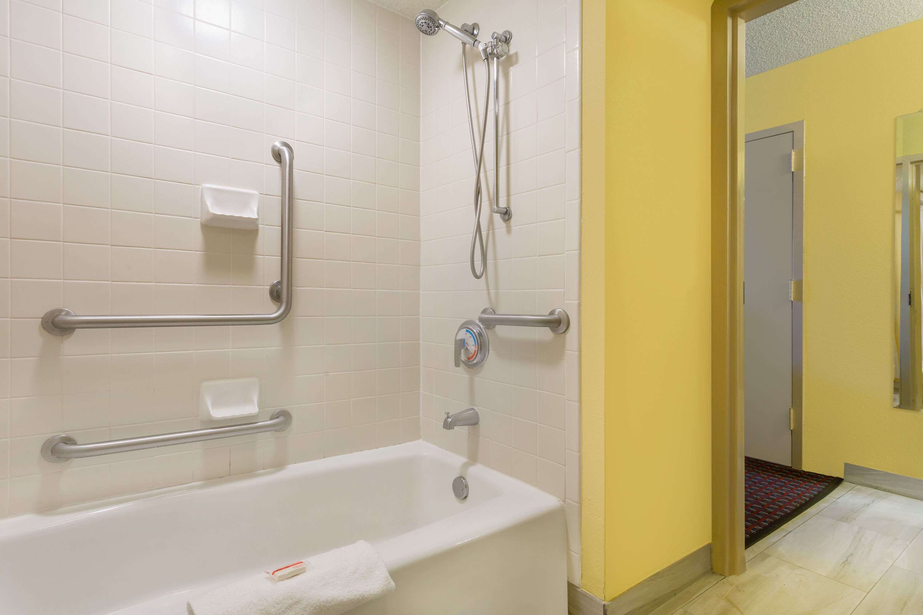A bathroom with a white bathtub, grab bars, a handheld showerhead, and a soap dish.