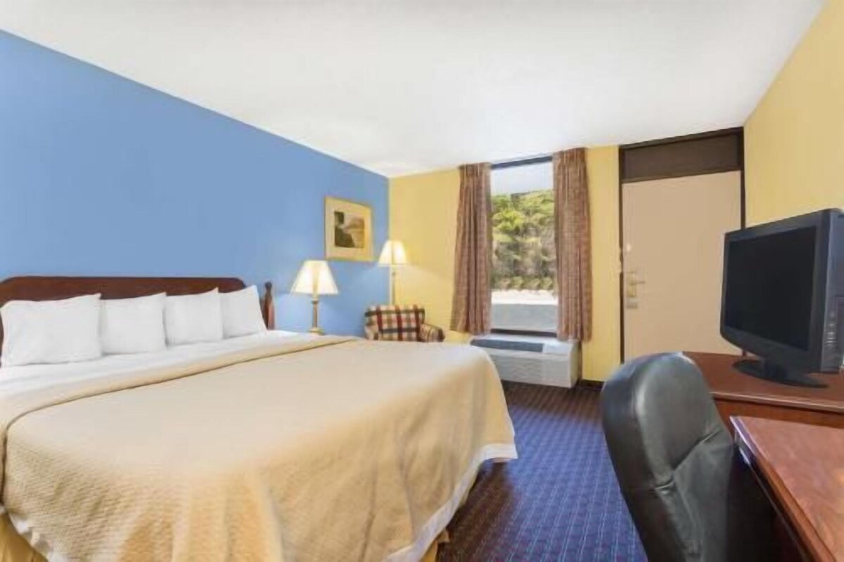 A hotel room with a bed, a desk with a computer, a chair, and a television.