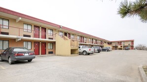 Un motel à étages, un parking avec plusieurs voitures et un petit escalier menant à l’entrée.