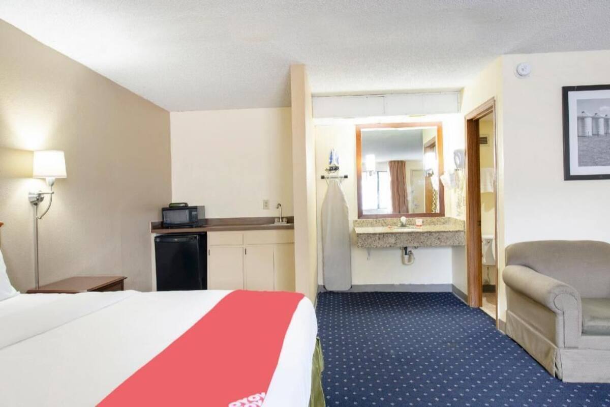 A hotel room with a bed, a desk, a kitchenette, a bathroom, and a chair.