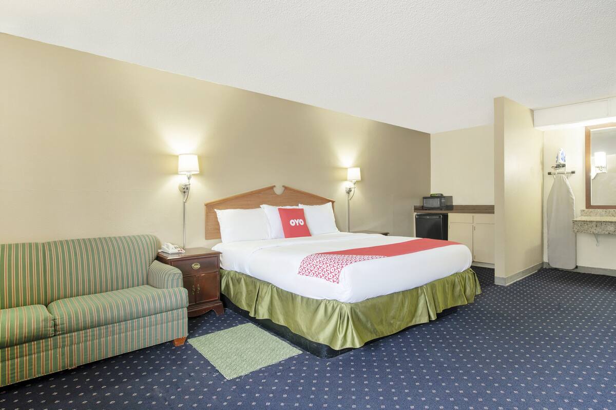 Una habitación de hotel con cama, un sofá verde a rayas, una mesita y un espejo.