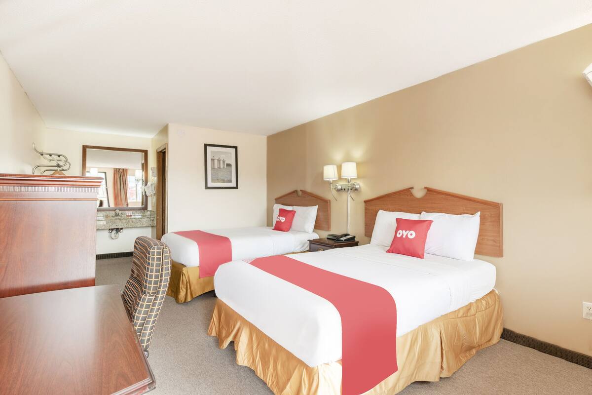 Una habitación de hotel con dos camas, un aparador de madera, una silla y un espejo.
