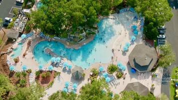 An aerial view of a resort with a large swimming pool, multiple lounge areas, and a covered pavilion.
